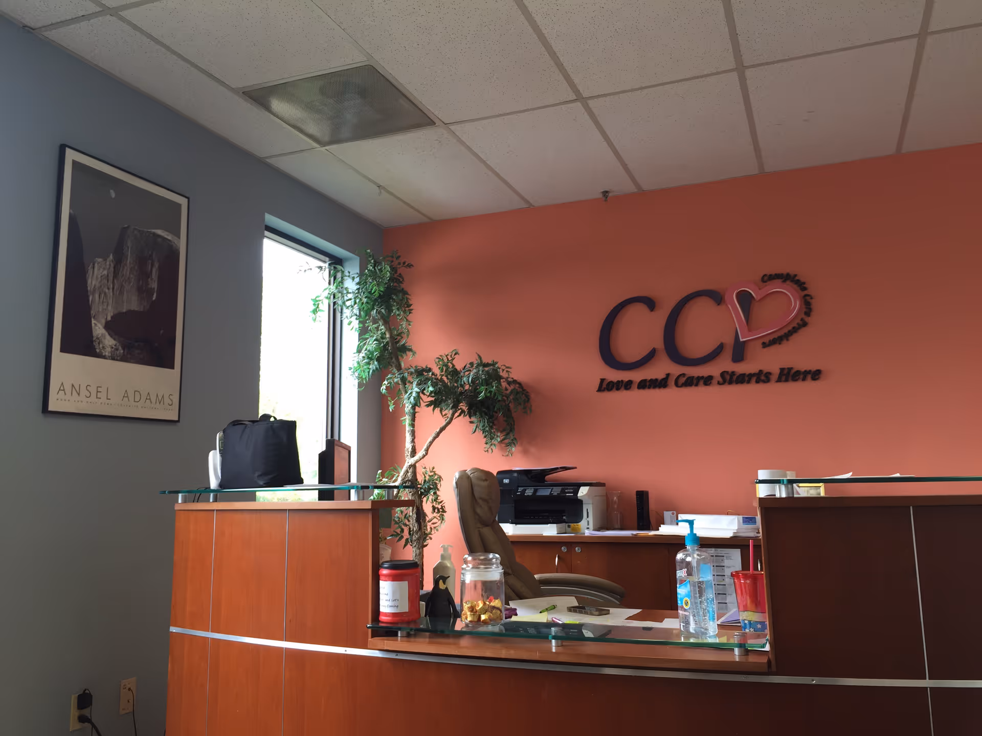 Reception desk in a facility lobby with a plant, logo wall, and framed art.