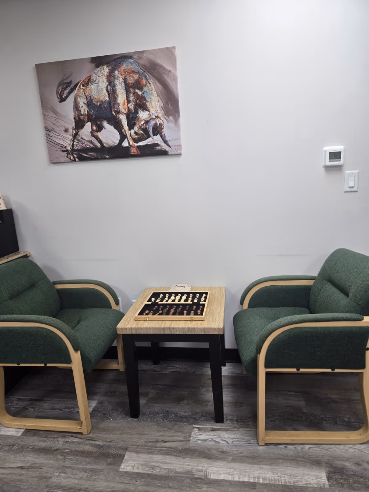 Two green armchairs frame a small table with a board game in a tidy lounge.