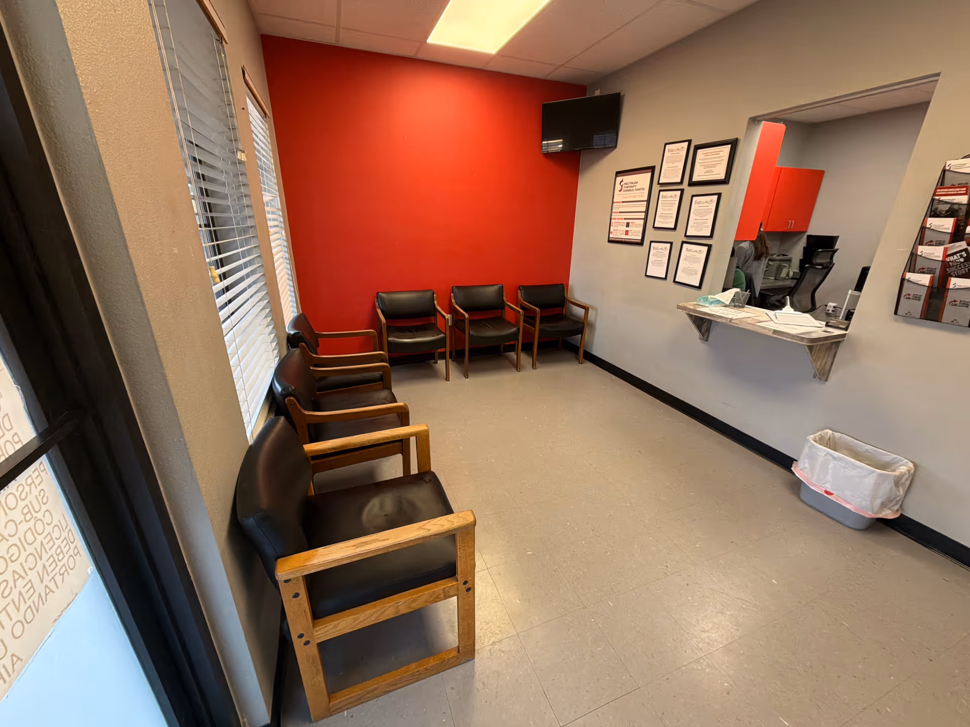 Reception area with red wall, row of chairs, and a front desk.