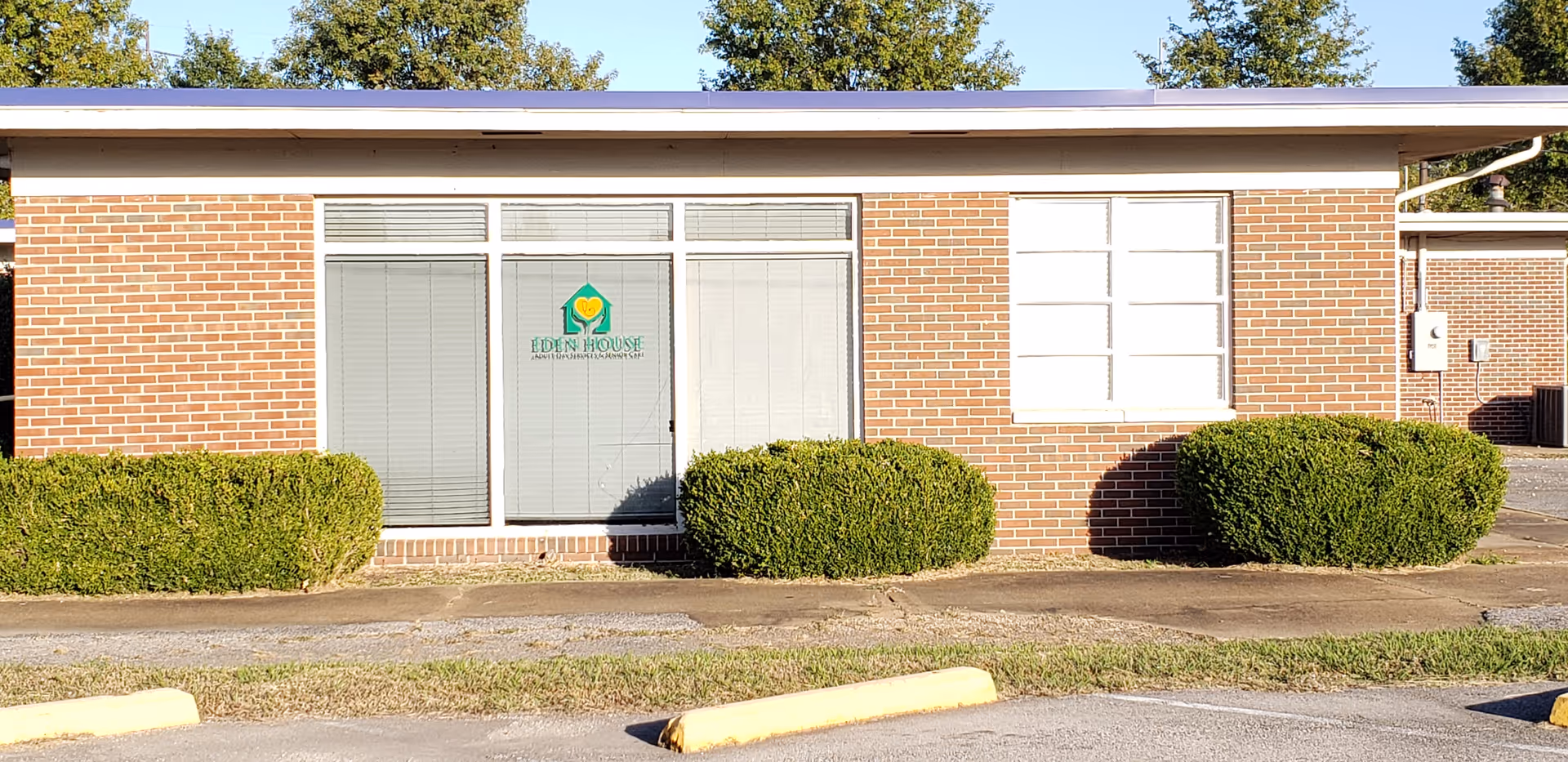 Brick facility exterior with large front windows and Eden House logo on entry door.
