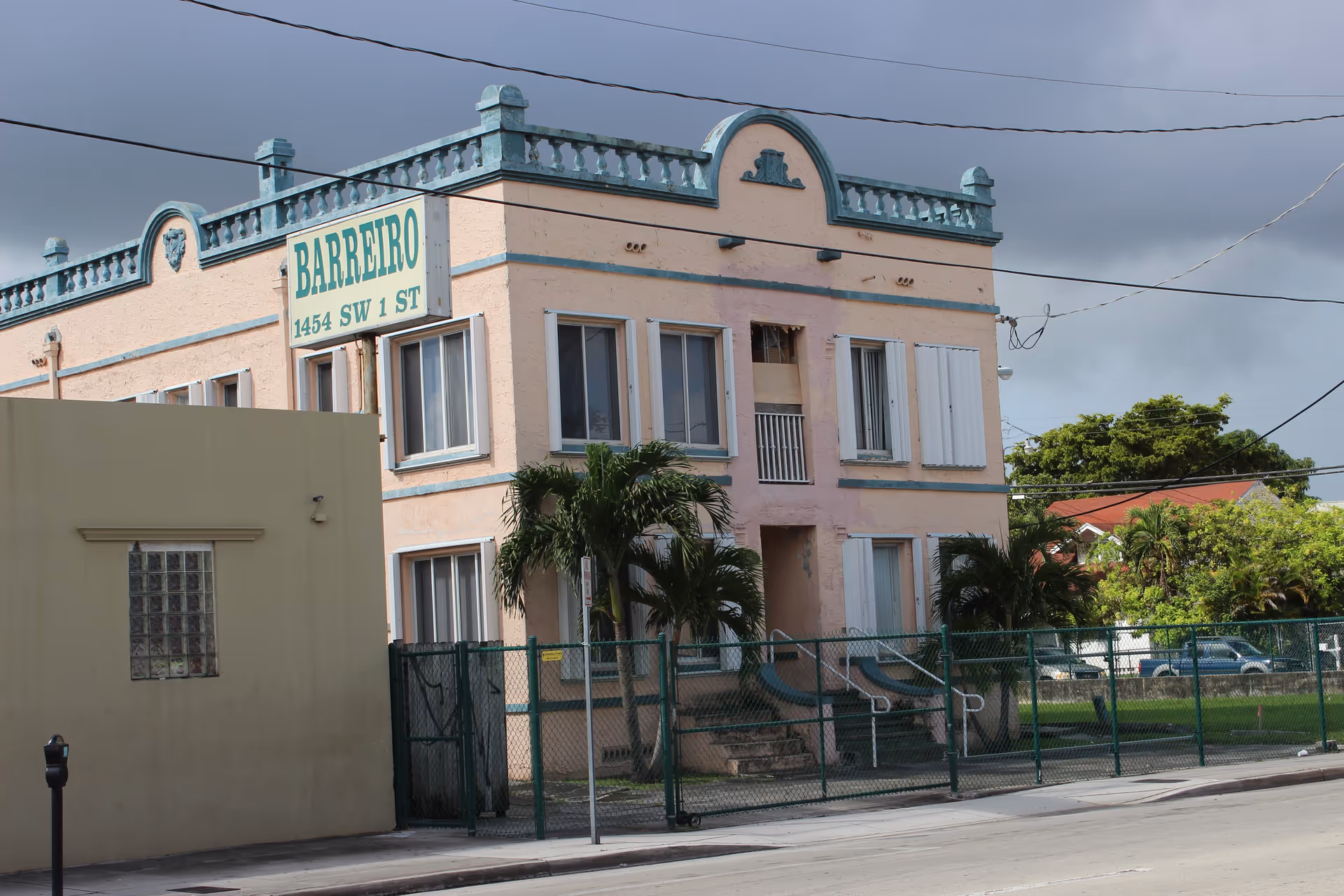 Two-story pink building with BARREIRO sign and a fenced front yard.