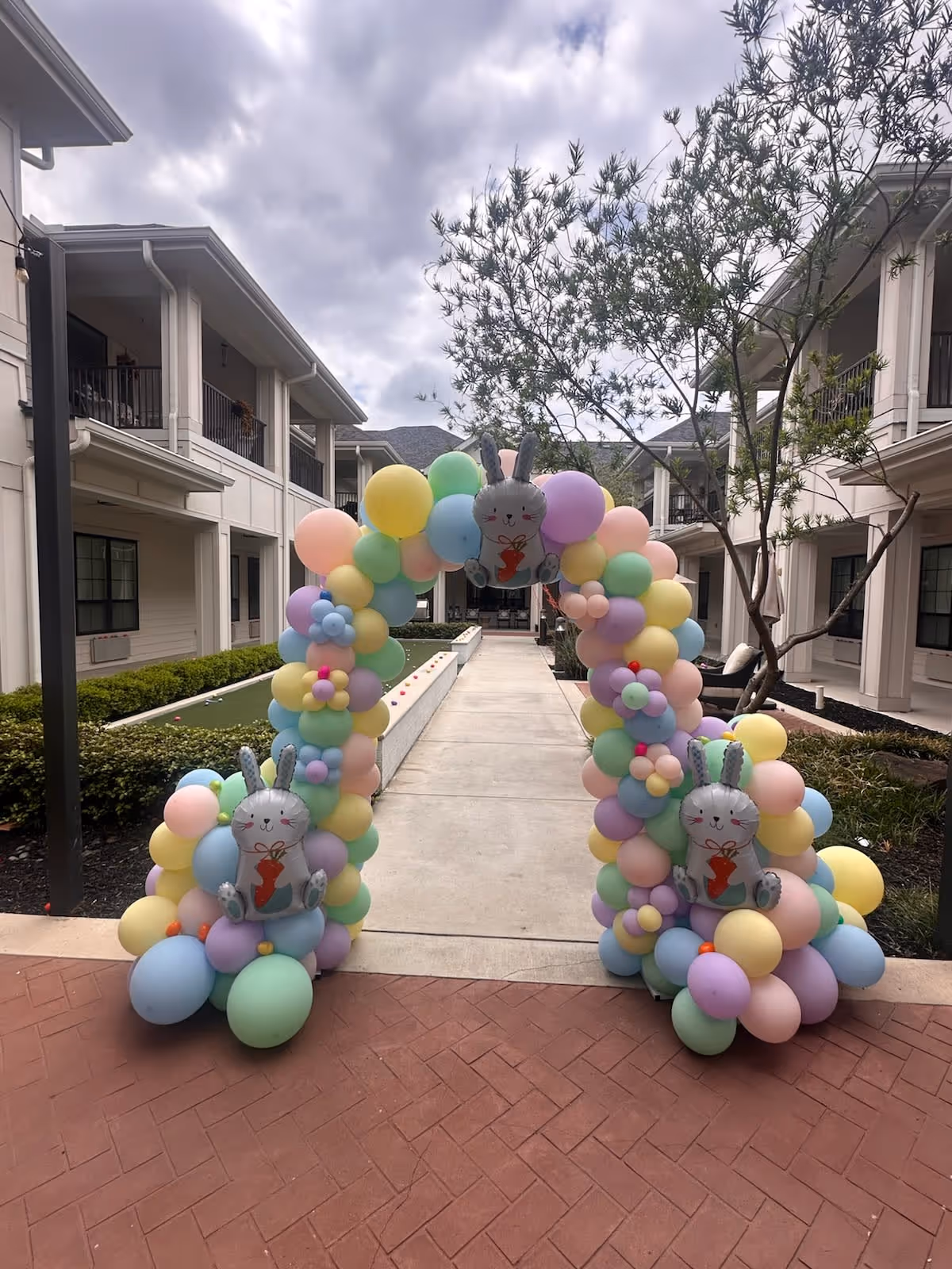 Pastel balloon arch with bunny decorations decorates an outdoor senior living courtyard.