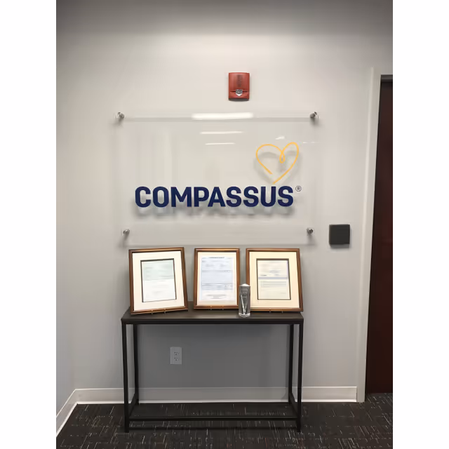 Interior hallway displays Compassus sign with framed certificates on a reception table.
