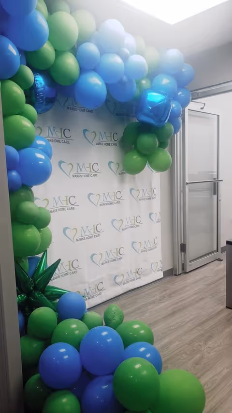 Interior hallway with a blue and green balloon arch around a branded MHC backdrop.