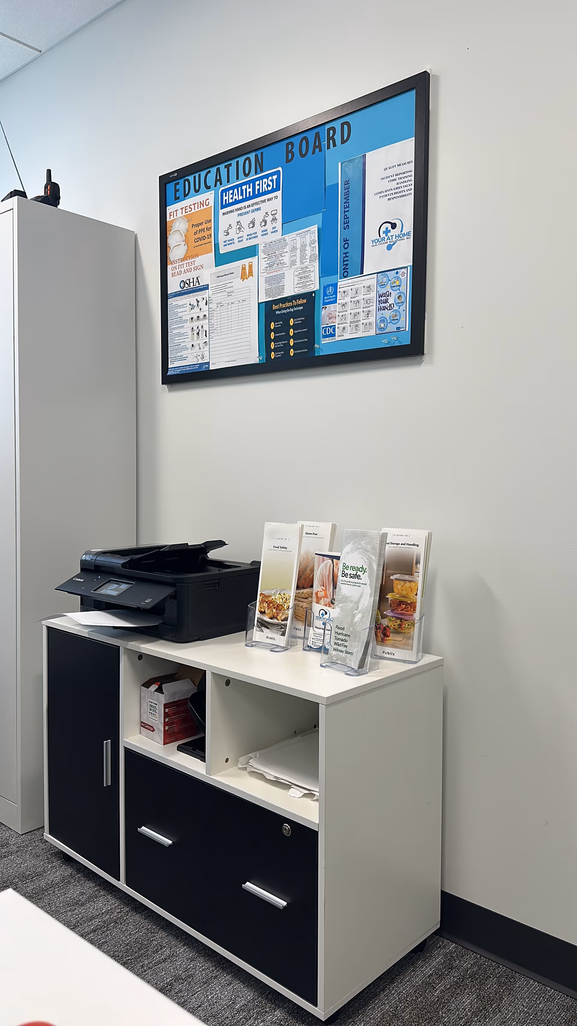 Interior office area with a printer on a white cabinet and an education bulletin board.
