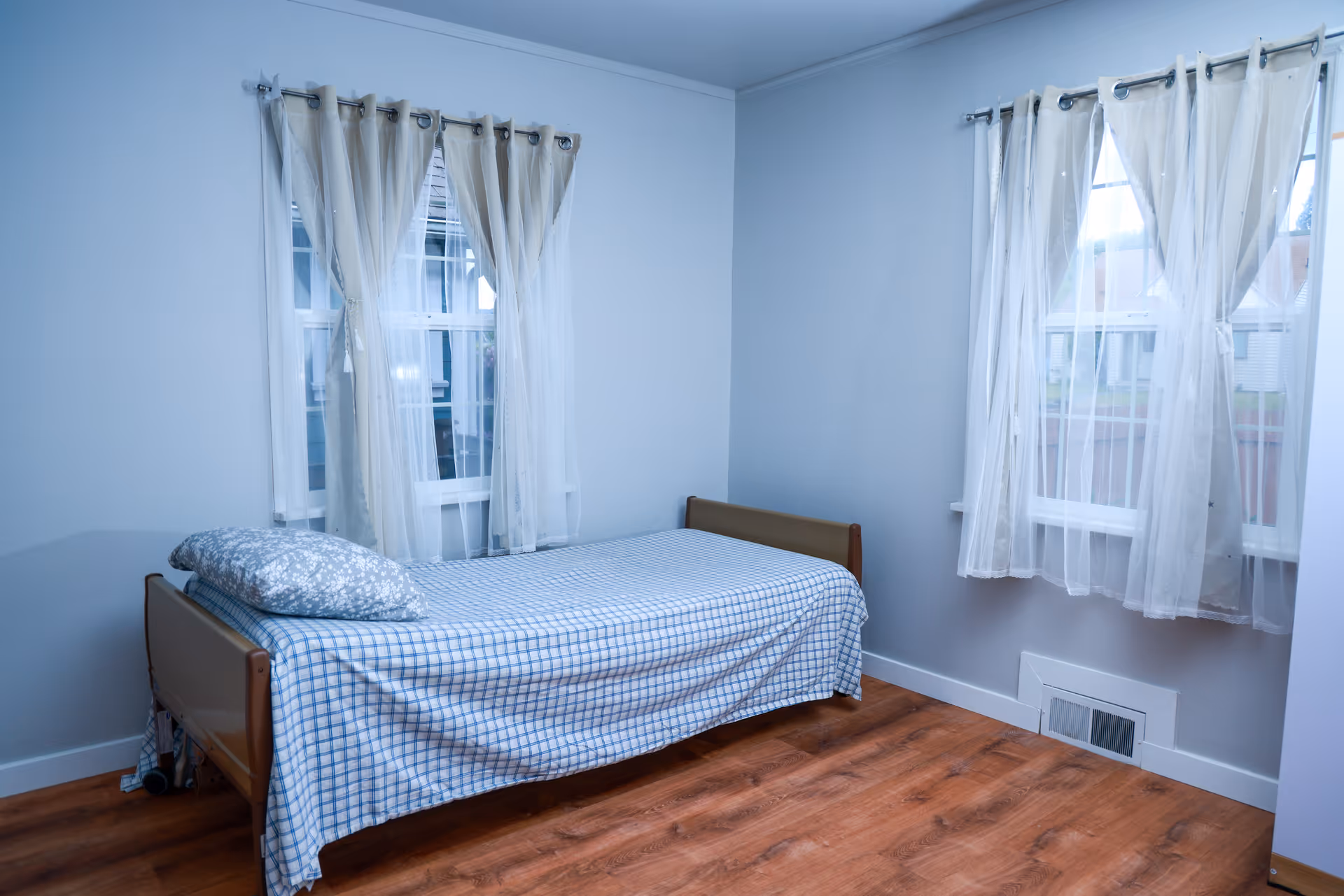 Simple bedroom in a care facility with a single bed and sheer curtains.