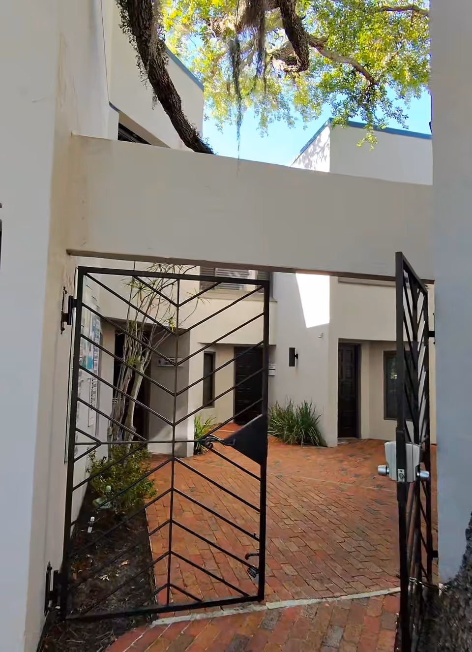 Exterior brick courtyard with a black metal gate and white building walls.