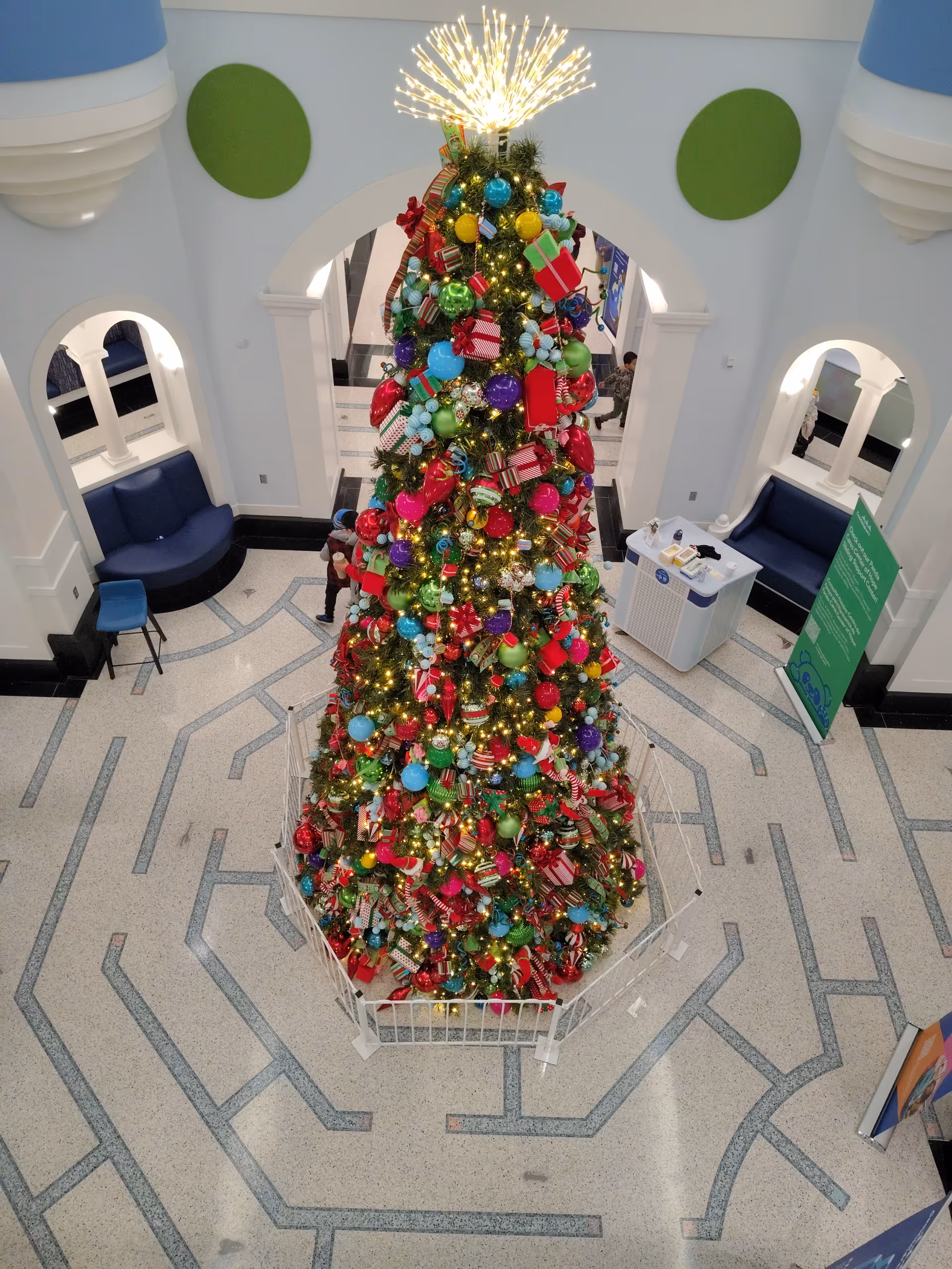 Large decorated Christmas tree inside a bright medical facility lobby with arches.