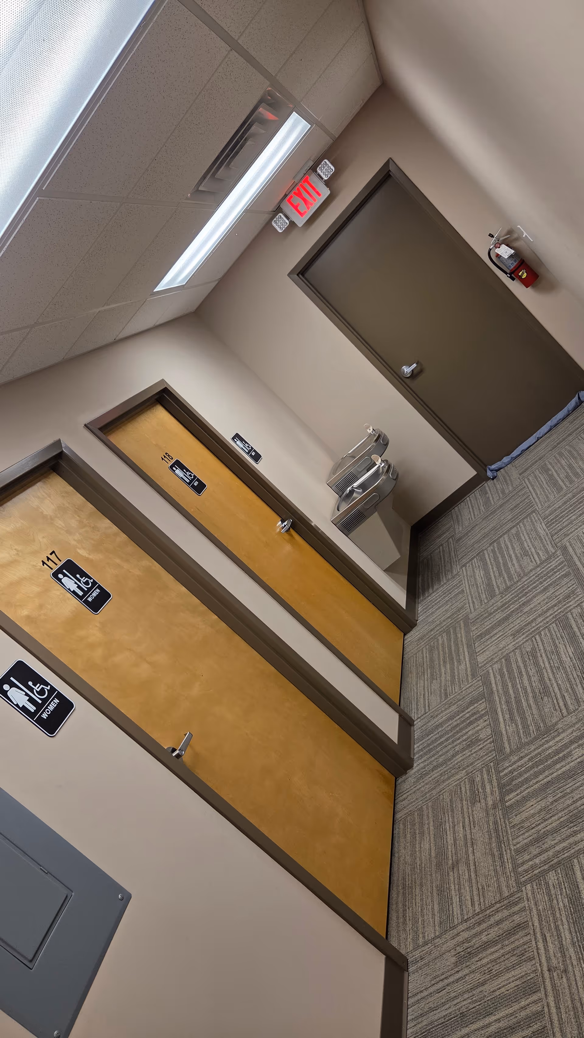 Interior hallway with numbered doors, exit sign, and fire extinguisher in a senior facility.