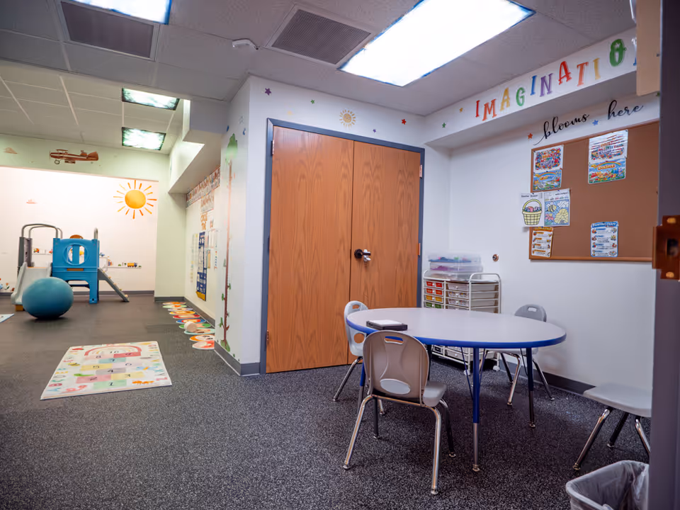 Colorful therapeutic playroom with a round table, chairs, rug, and soft play equipment.