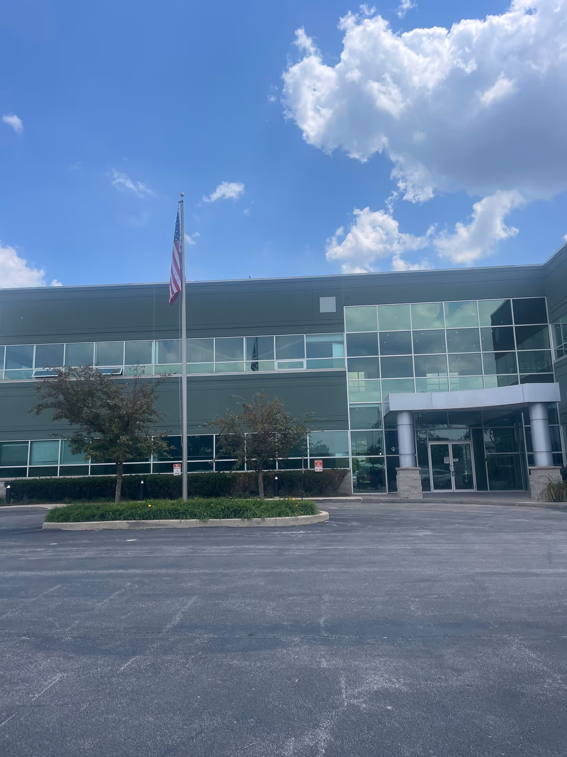 A modern glass-front senior living facility exterior with a flagpole and main entrance.