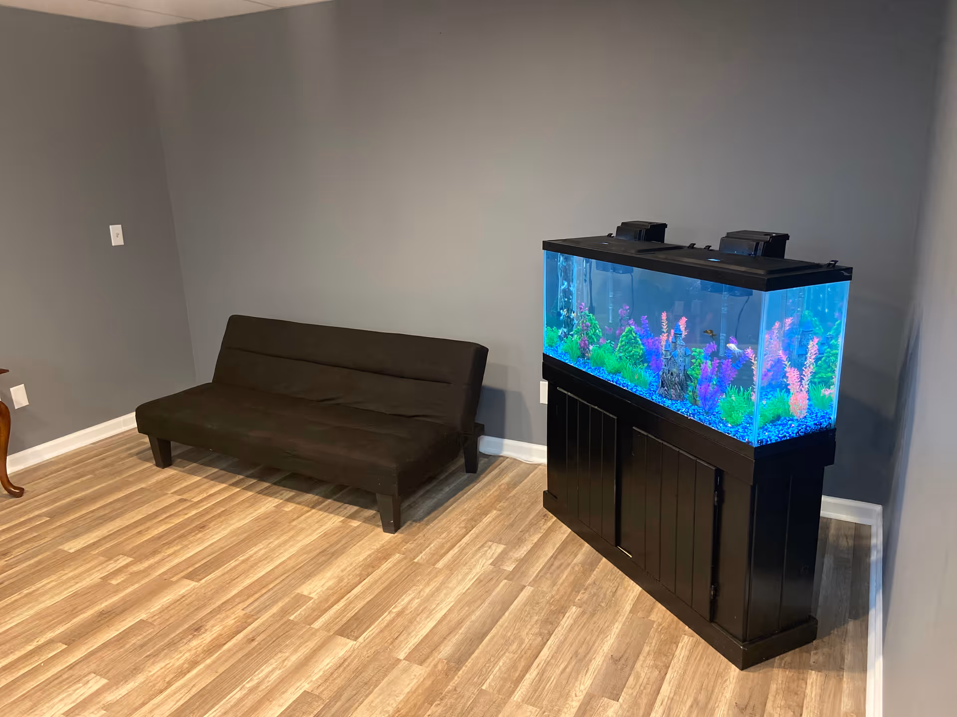 A dark sofa sits beside a large aquarium on a black stand.