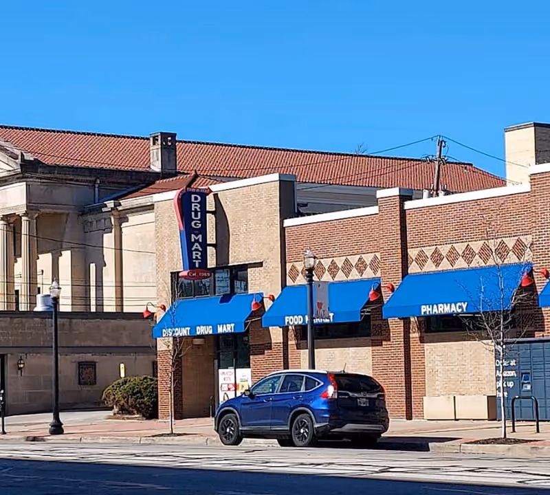Brick building with blue awnings and Discount Drug Mart signage on a city street.