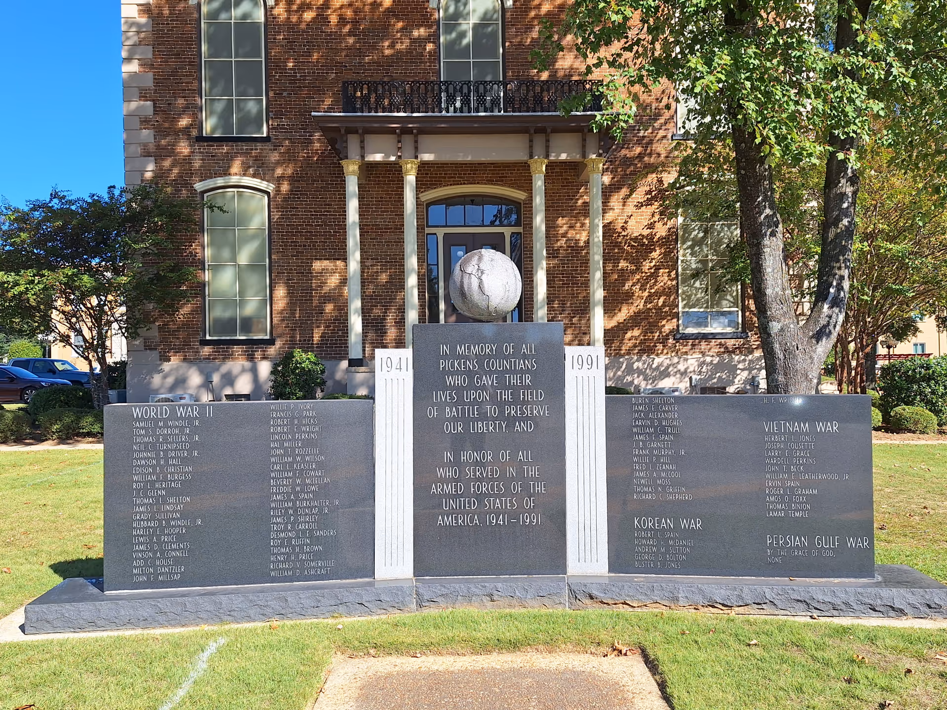 Brick building with columns and a three-panel memorial stone display in front.