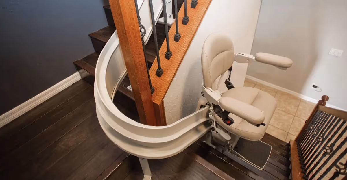 Curved staircase with a beige stair lift chair installed beside the railing.