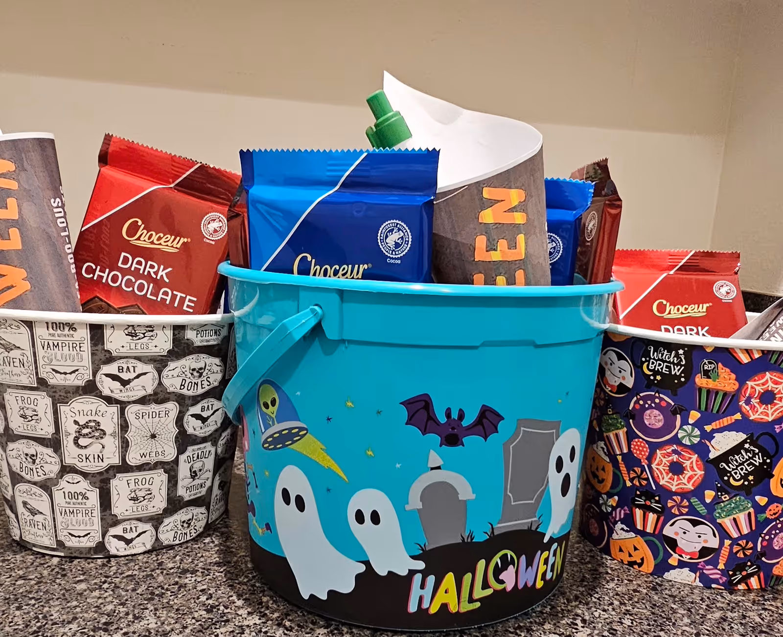 Bright blue Halloween-themed bucket filled with assorted snack bags on a counter.