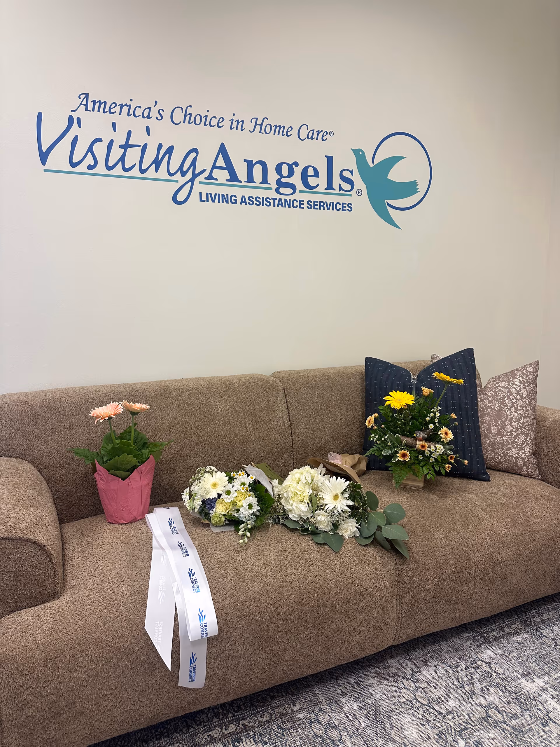Brown sofa beneath Visiting Angels logo with flower bouquets on the seat.
