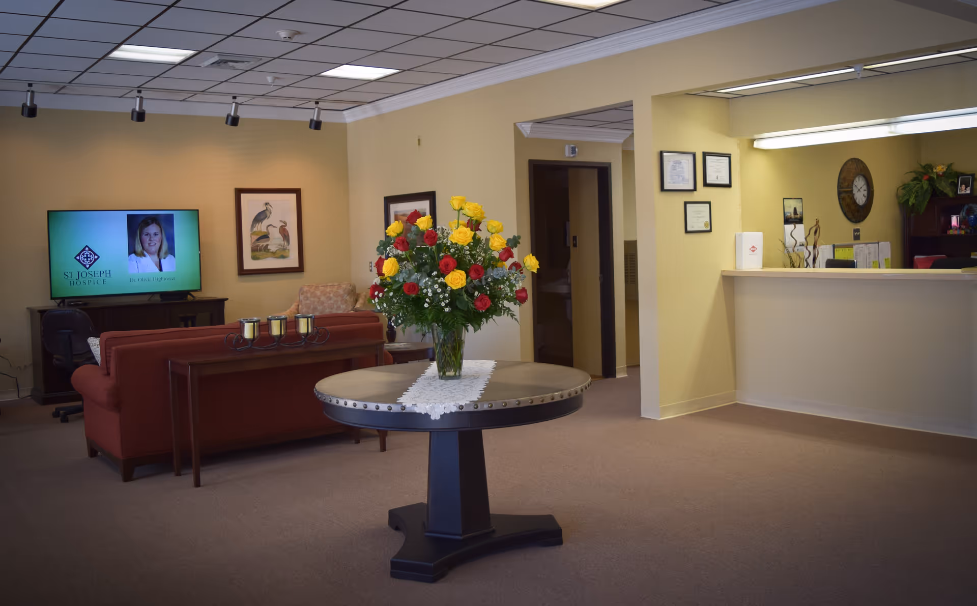 Lobby seating area with sofa, round table, flowers, and a reception desk.