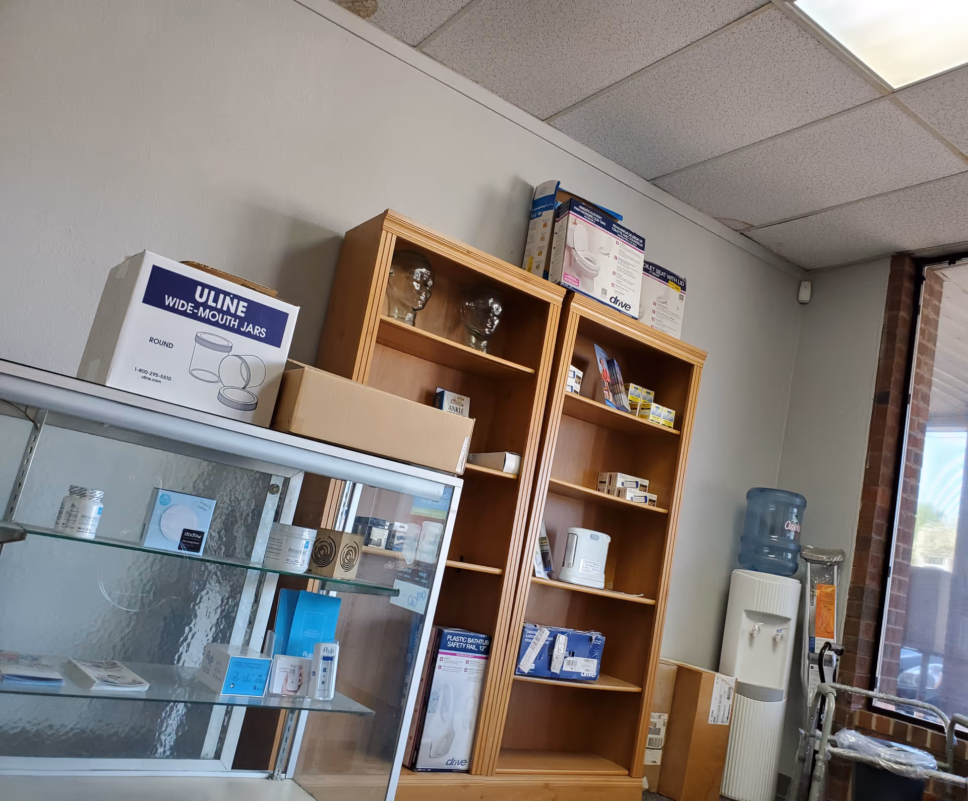 Interior of a facility supply room with wooden shelves of medical items and a water cooler.