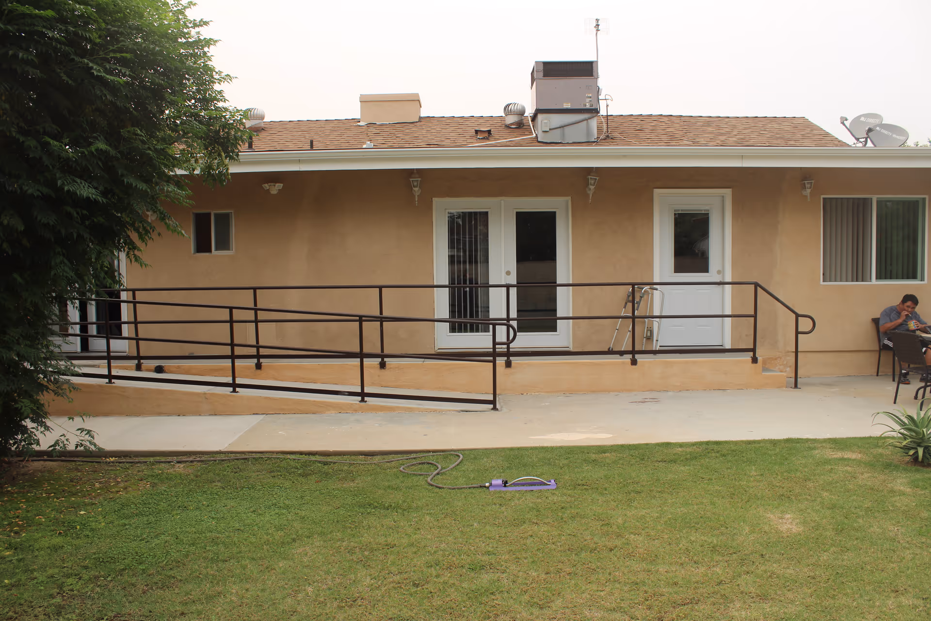 Exterior view of Aramat Board and Care with ramp, beige walls, and a person seated outside.