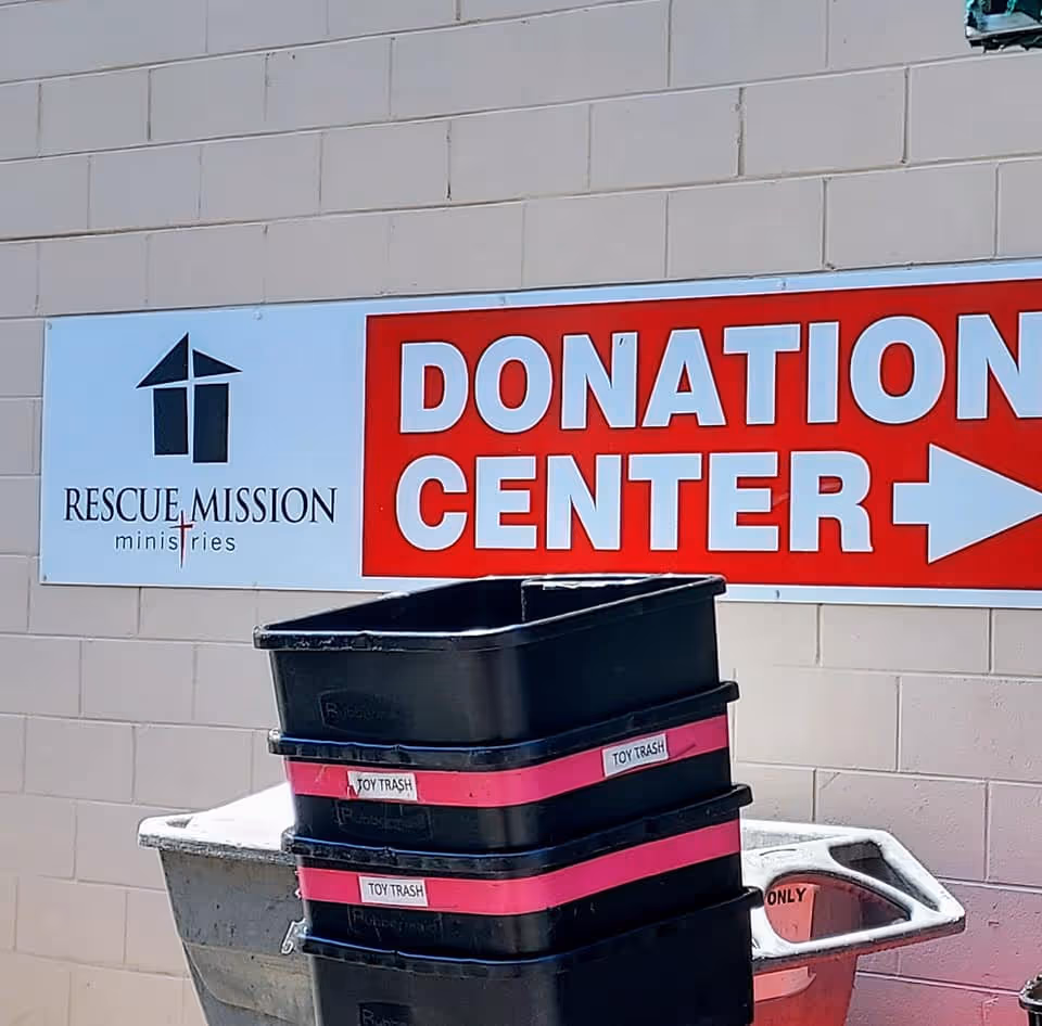 Outdoor wall featuring a large red donation center sign and stacked black trash bins.