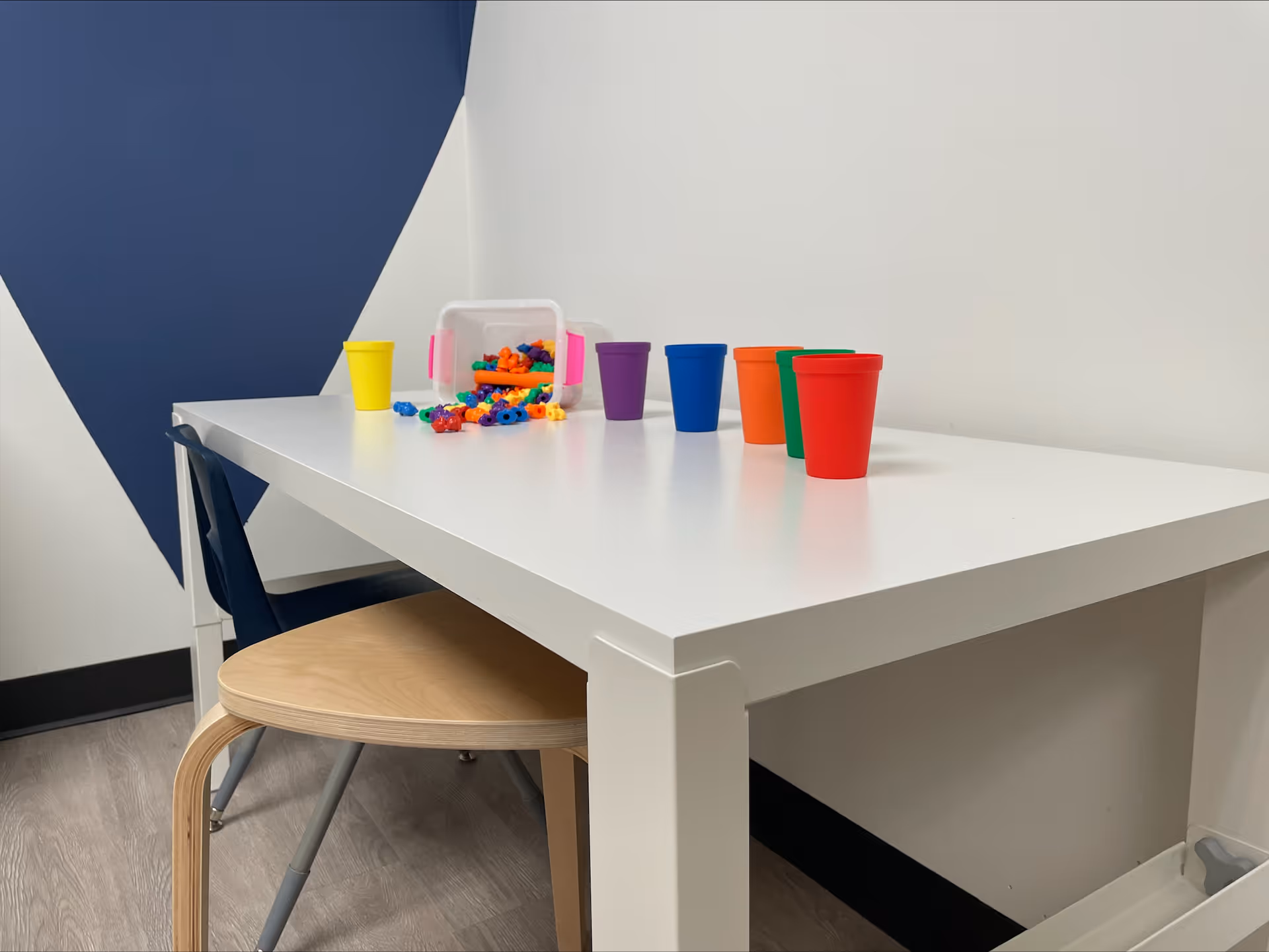 White table with colorful cups and plastic toys in a bright play area.