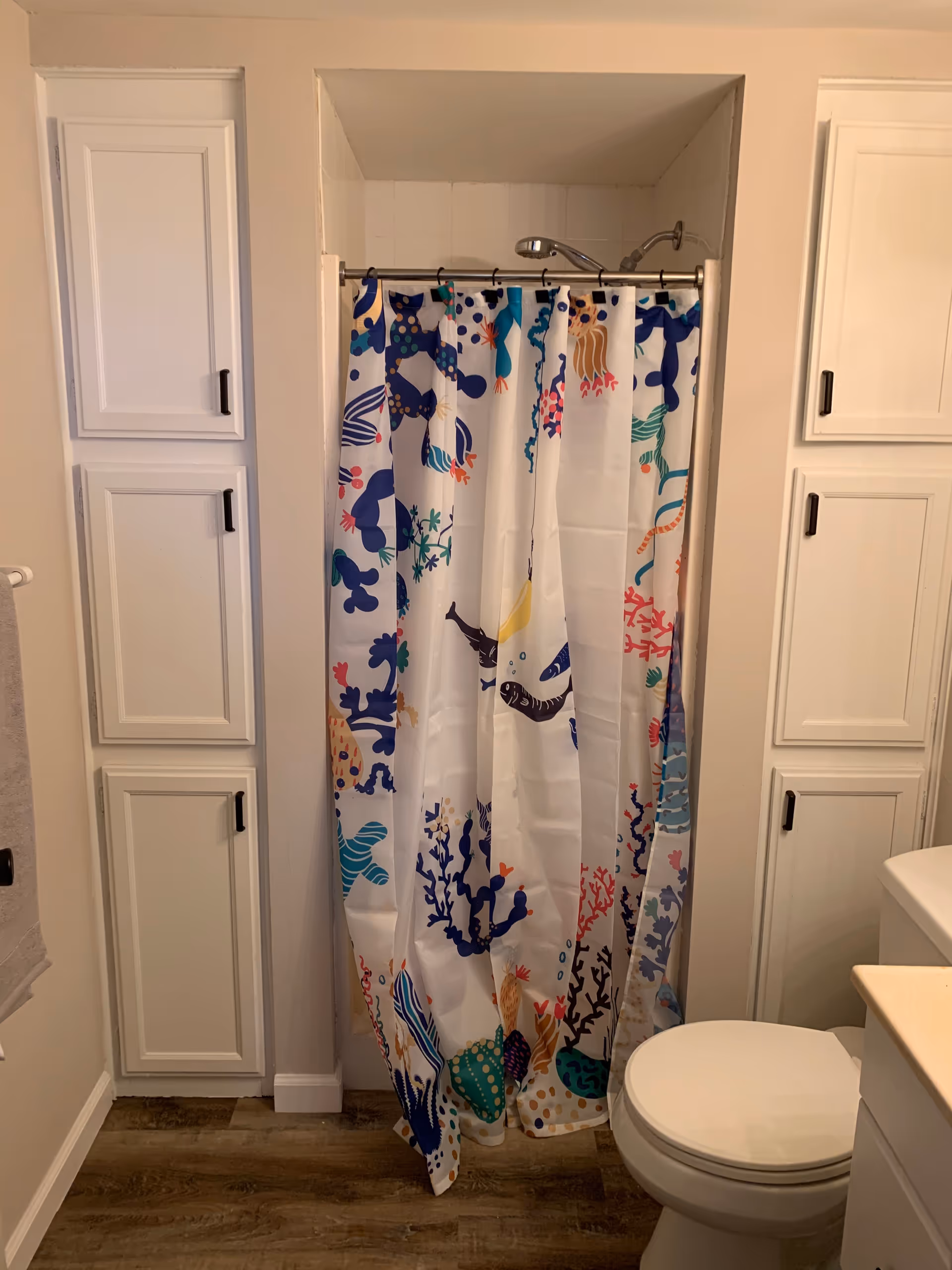 Bright bathroom with white cabinets, colorful shower curtain, and a toilet.