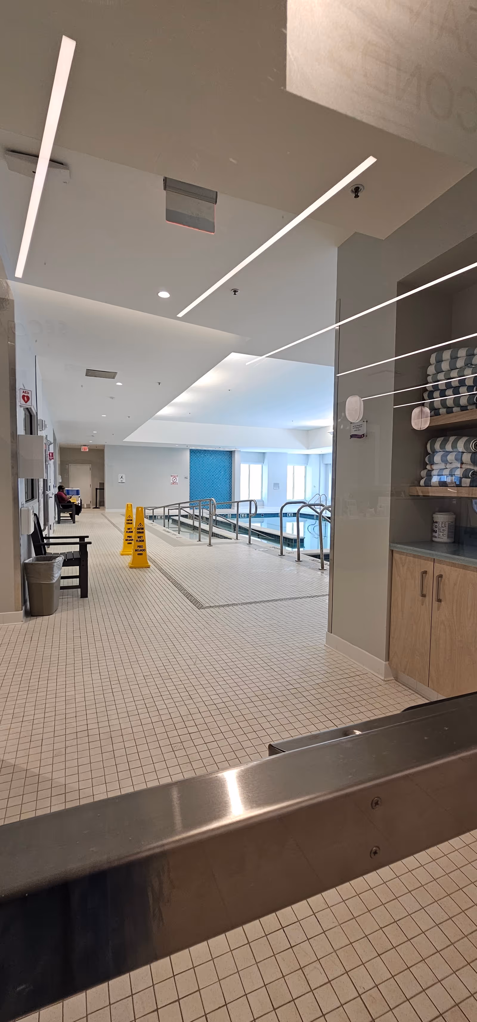 Indoor pool area with tiled floor, handrails, and towels on shelves.