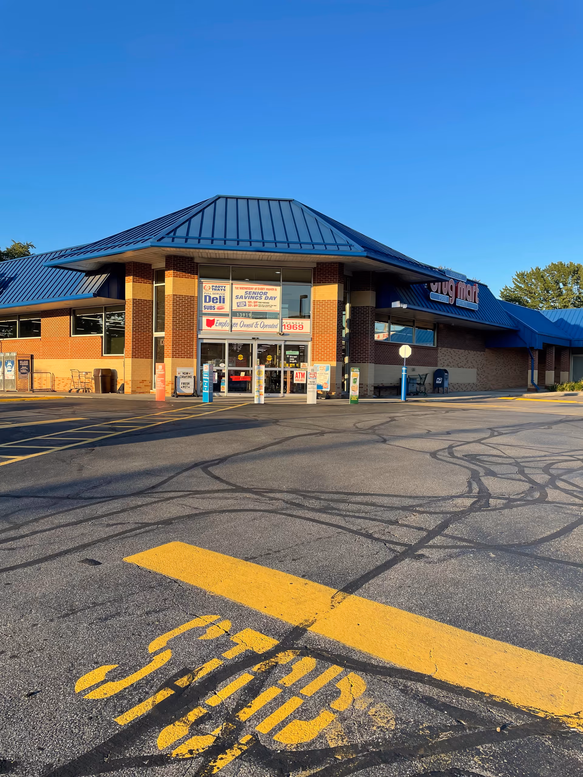 Exterior view of a Discount Drug Mart storefront with blue metal roof and parking lot.