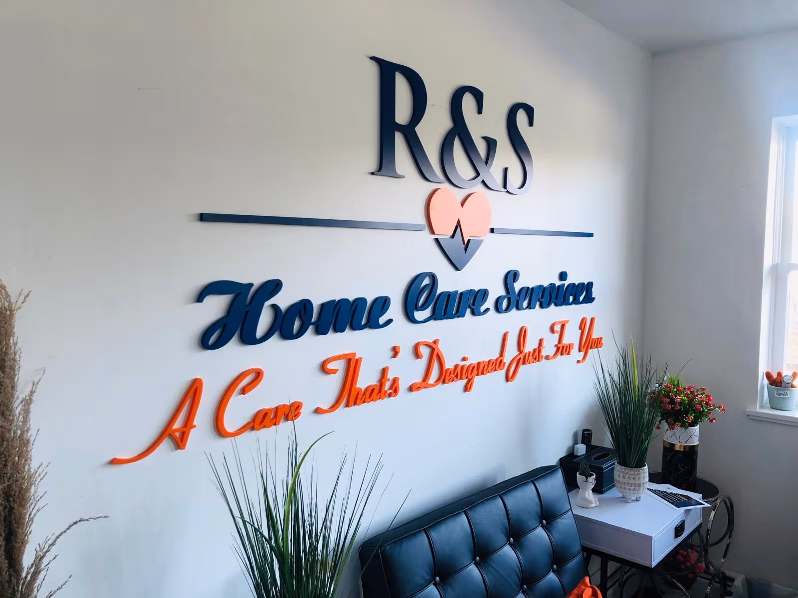Interior wall displays R&S Home Care Services sign with plants and a couch.