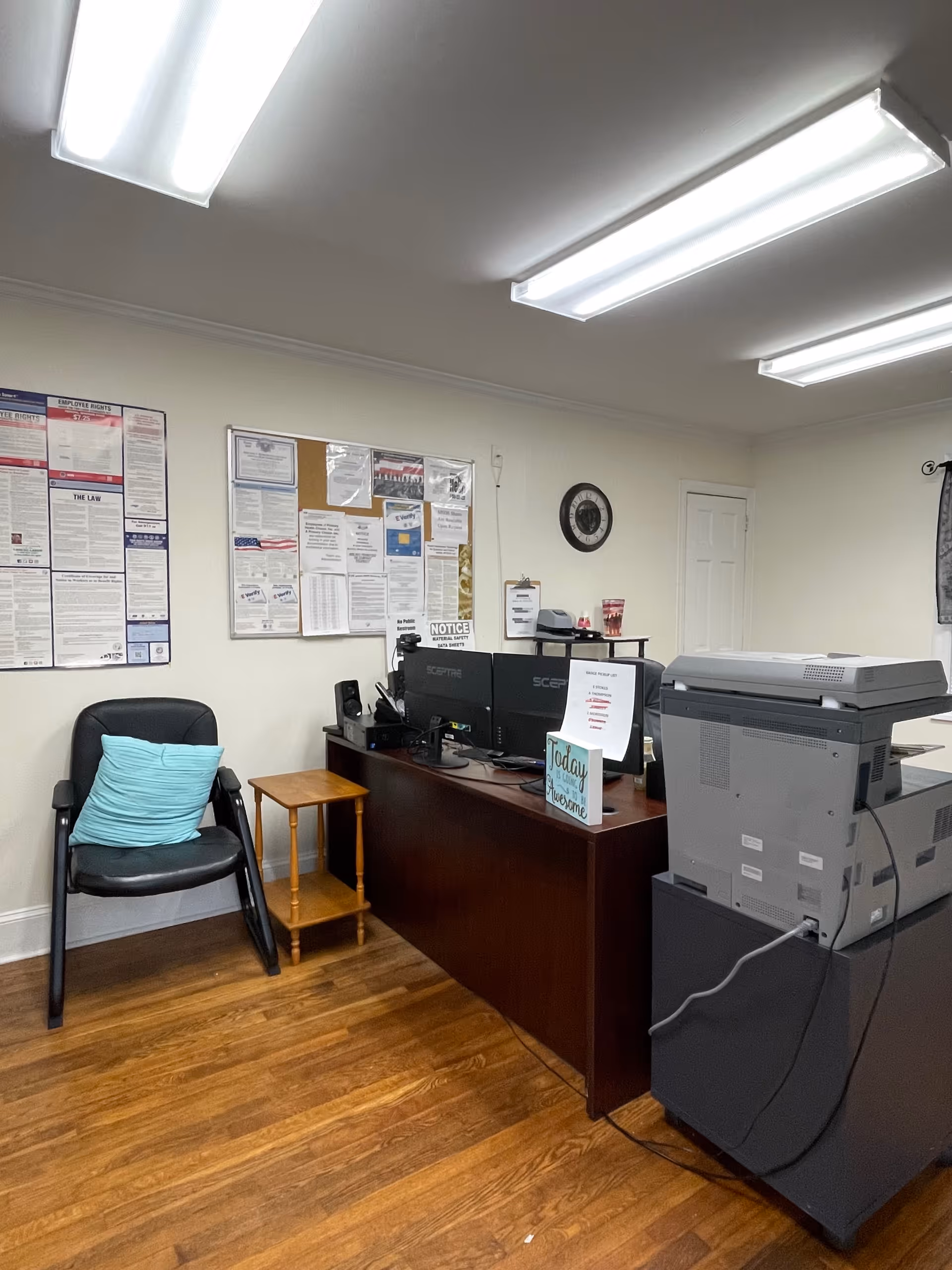 Office area with desk, computers, printer, bulletin boards, and a chair in a senior facility.