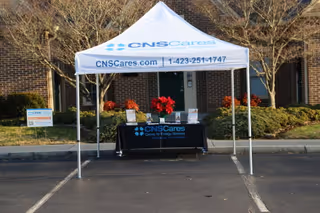 A CNS Cares information tent with a display table sits in a parking lot outside.