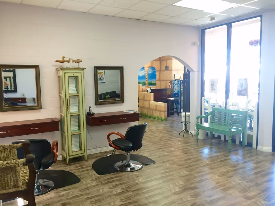 Interior salon area with mirrors, chairs, a green cabinet, and an arched doorway.