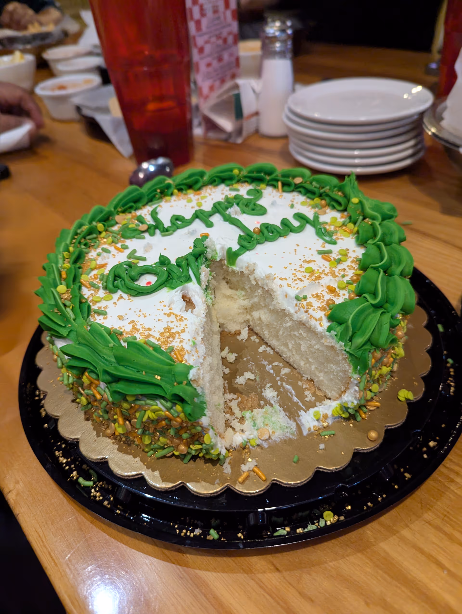 A white cake with green icing and sprinkles on a wooden dining table.
