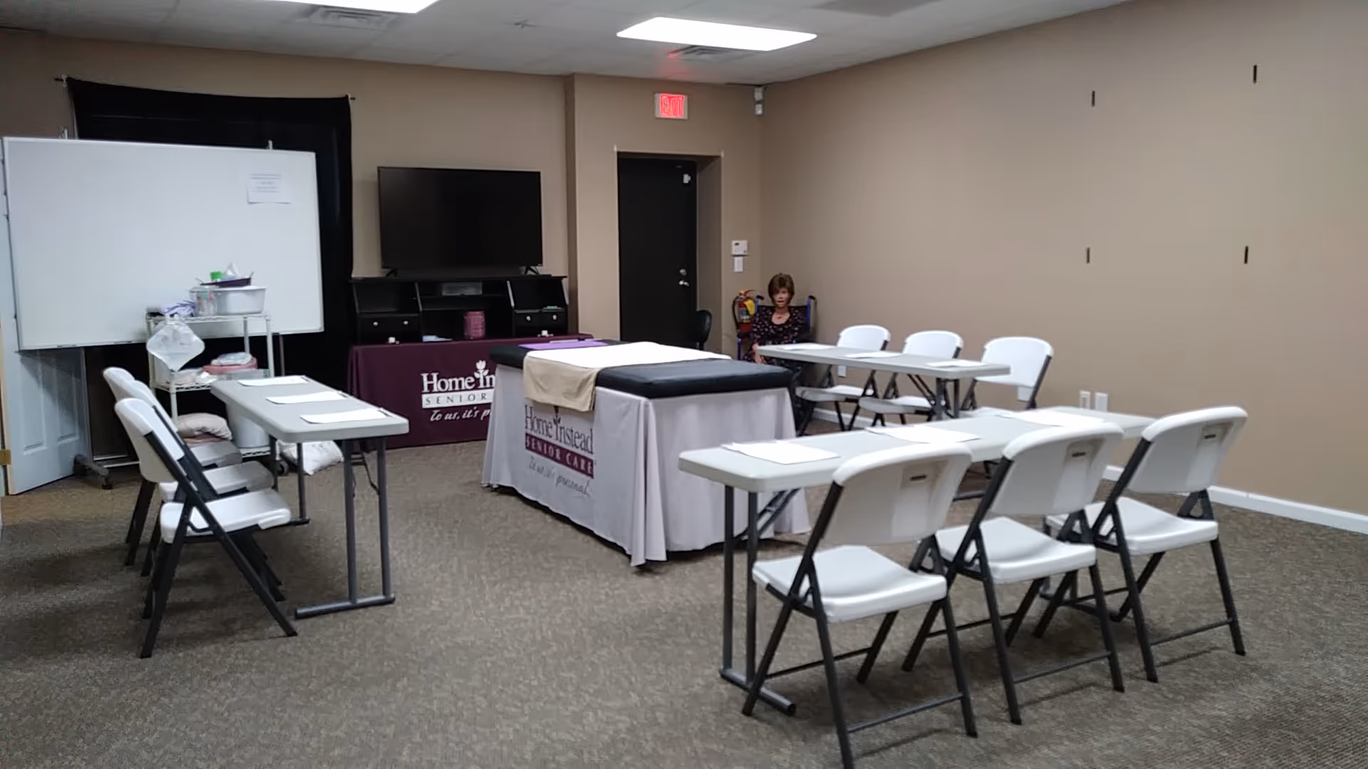 Training room setup with folding chairs, tables, whiteboard, TV, and Home Instead banners.