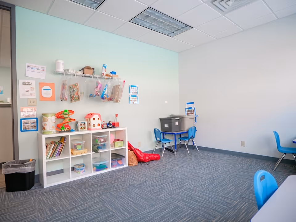 Bright children's play area with cubby shelves, toys, and blue chairs.