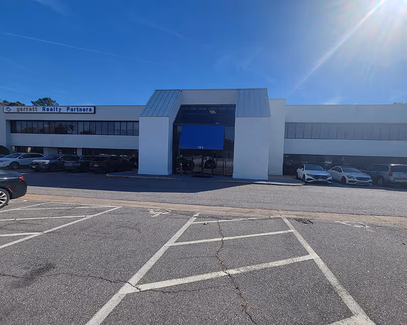 White corporate-style building with blue entrance awning and parked cars in a sunny lot