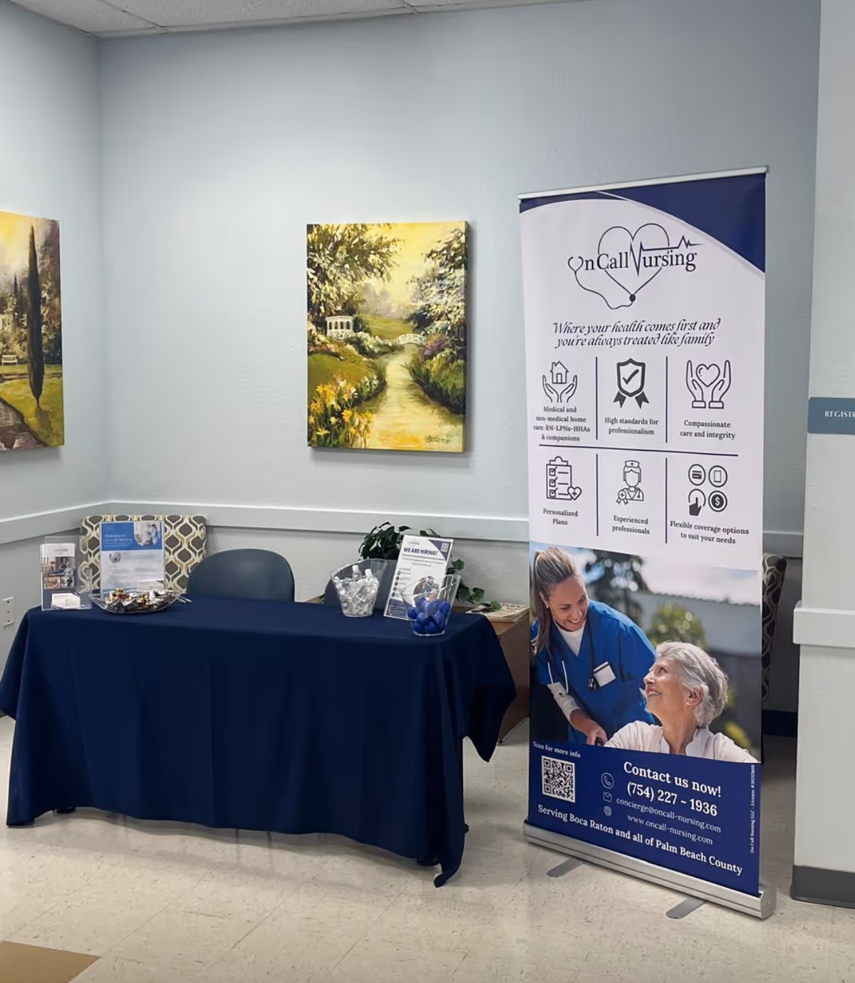 An indoor reception area with a navy table, chairs, paintings, and a promotional banner.