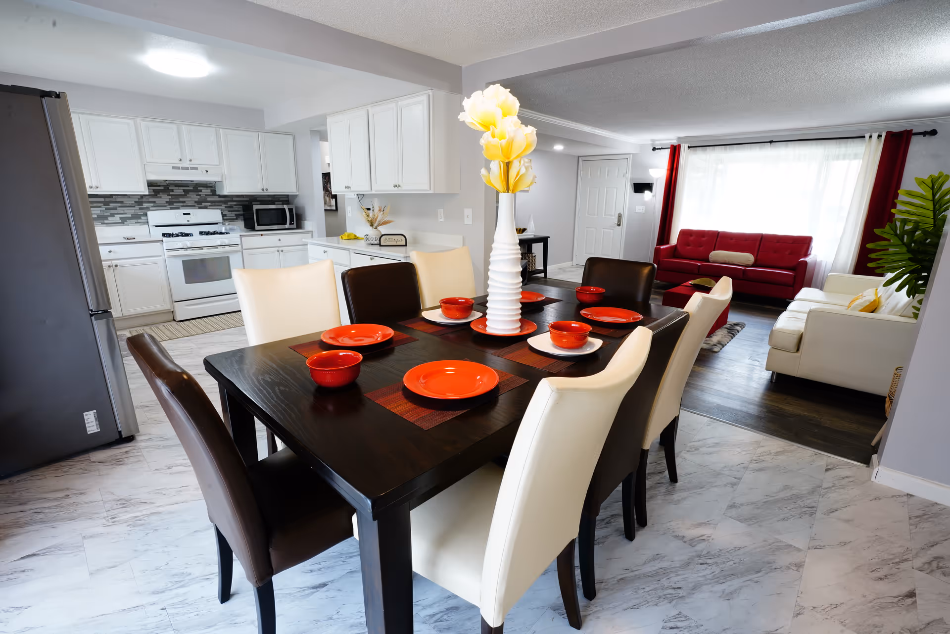 Open-concept dining area with a dark table, red dishes, white chairs, and connected kitchen.