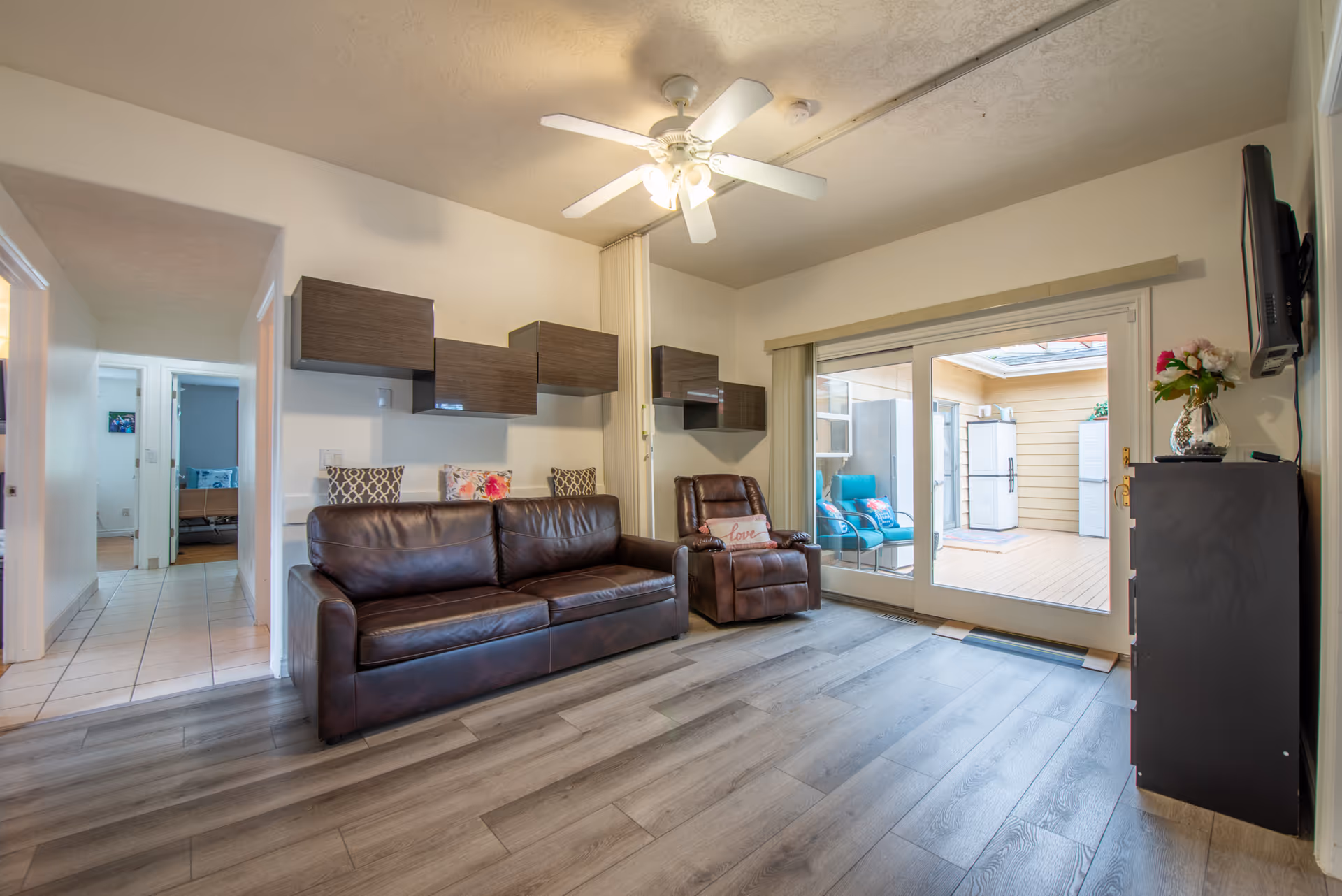 Cozy living room with leather sofa, recliner, ceiling fan, and sliding door to patio.