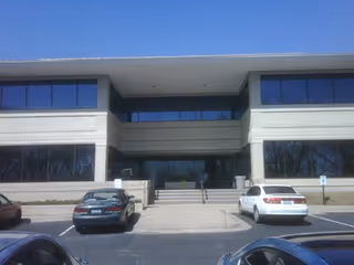 Front view of a two-story beige building with large windows and a parking lot.