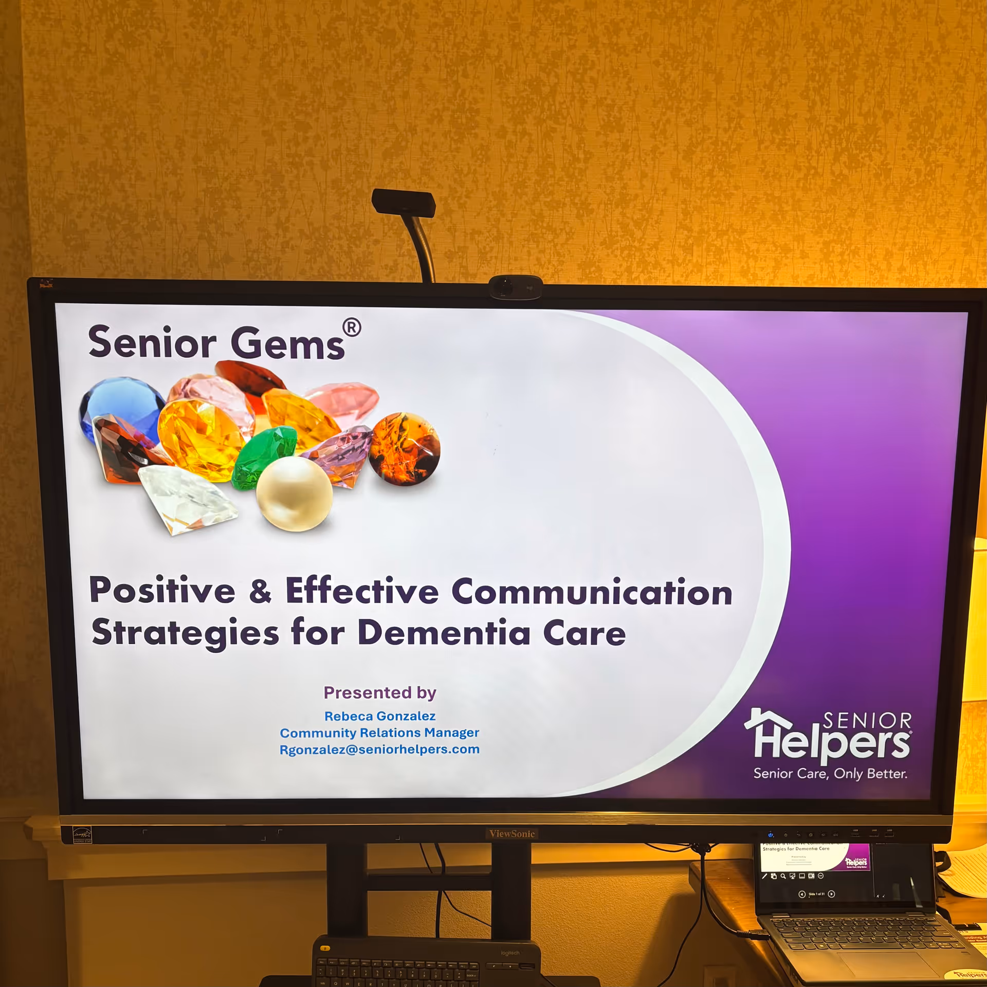 Indoor screen shows Senior Gems slide on dementia care with Senior Helpers logo.