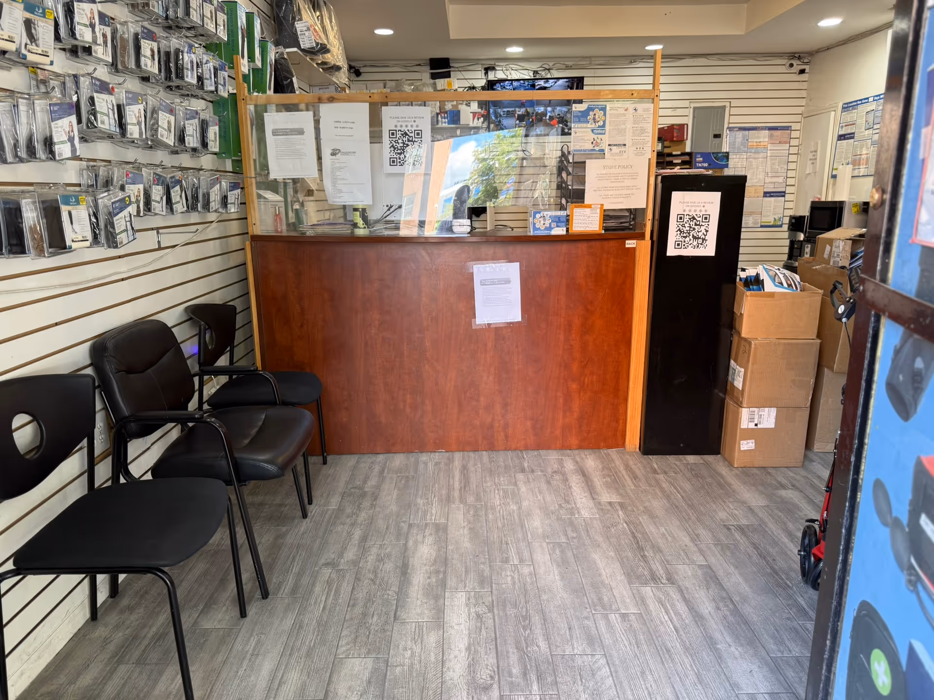 Inside Galaxy Medical Supply, a reception counter with wooden front, black chairs, and stacked boxes.