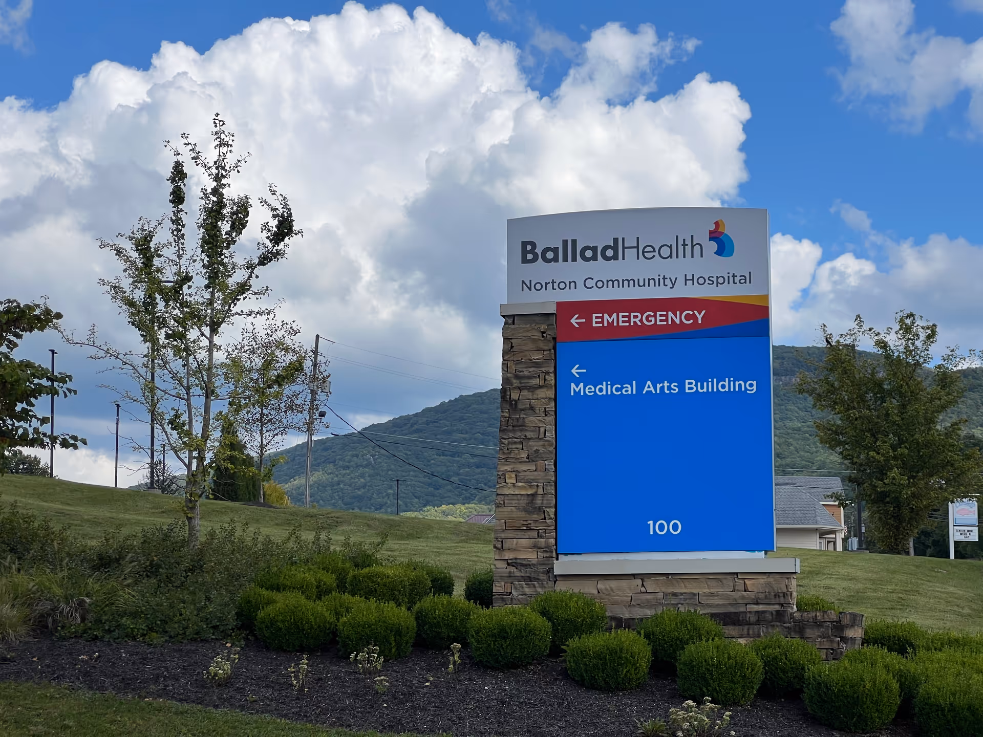 Exterior view of Ballad Health Norton Community Hospital sign with blue sky and landscaped grounds.