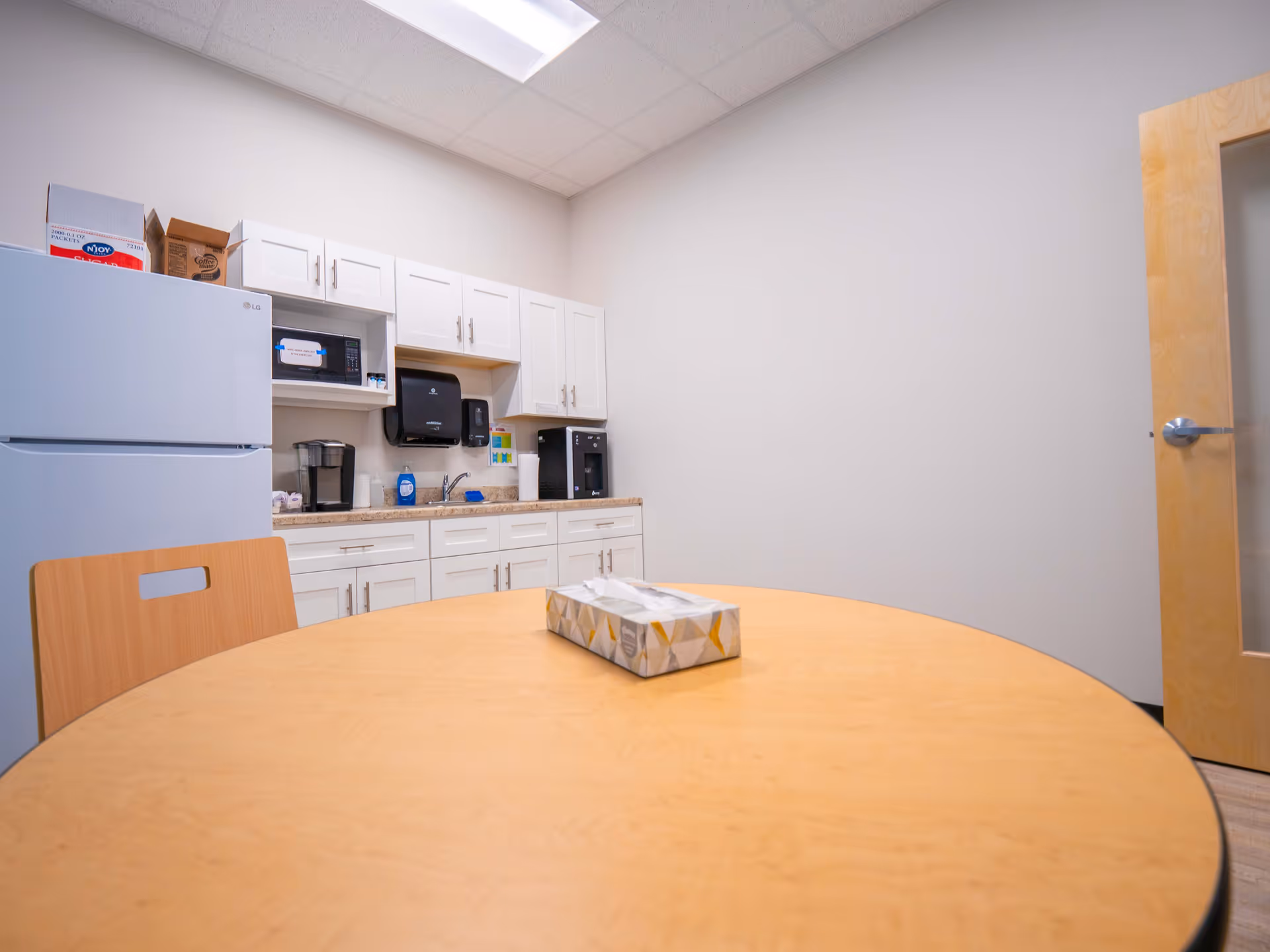 Bright kitchenette with white cabinets, a round wooden table, and assorted appliances.