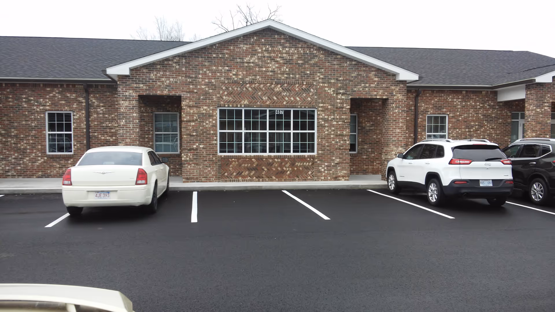 Brick building front with a parking lot and several cars.