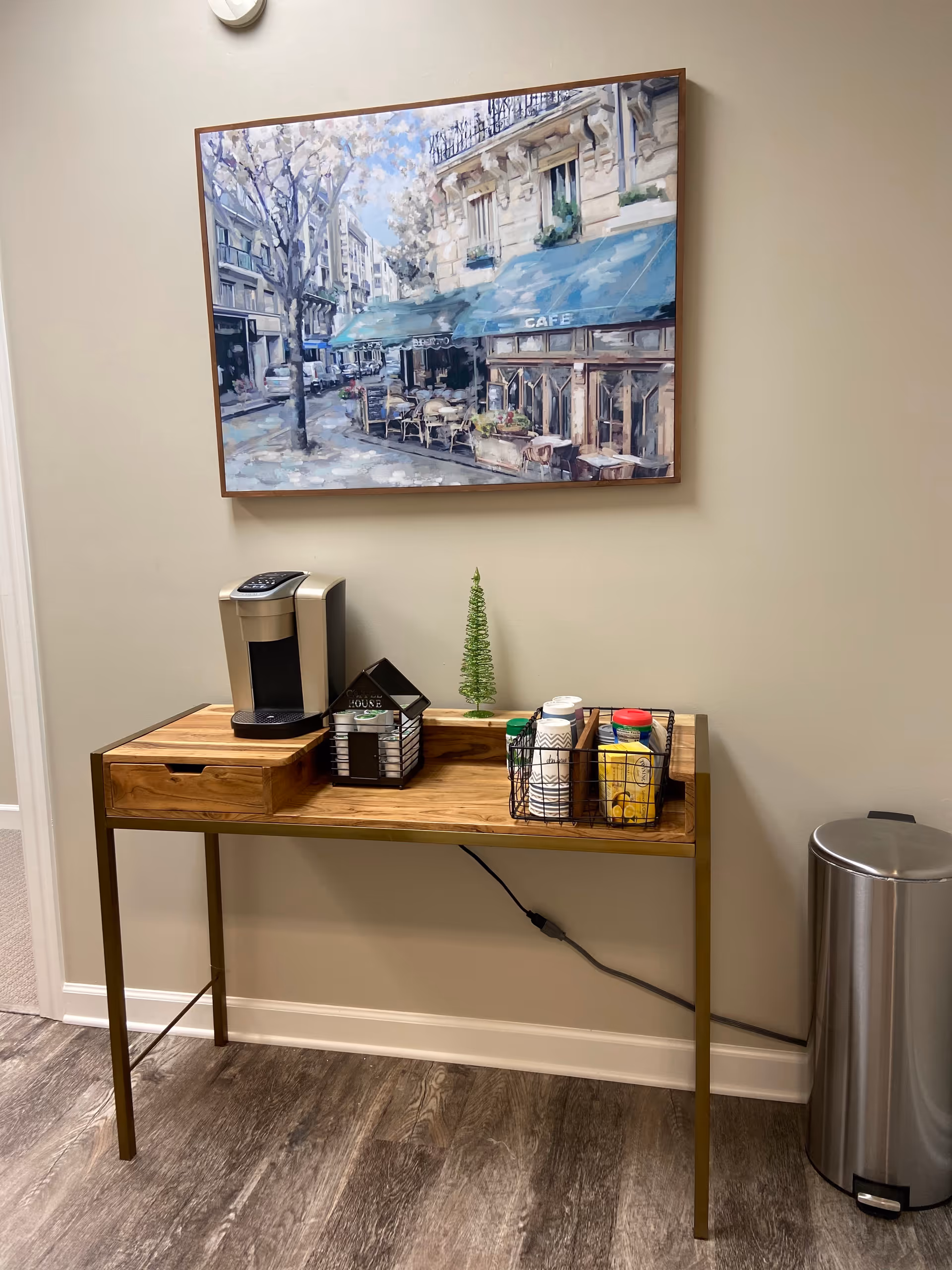 Wooden coffee station on a beige hallway wall with a painting above.