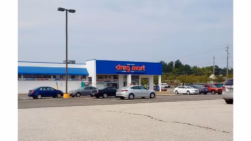 Front view of Discount Drug Mart store with blue sign and parked cars.