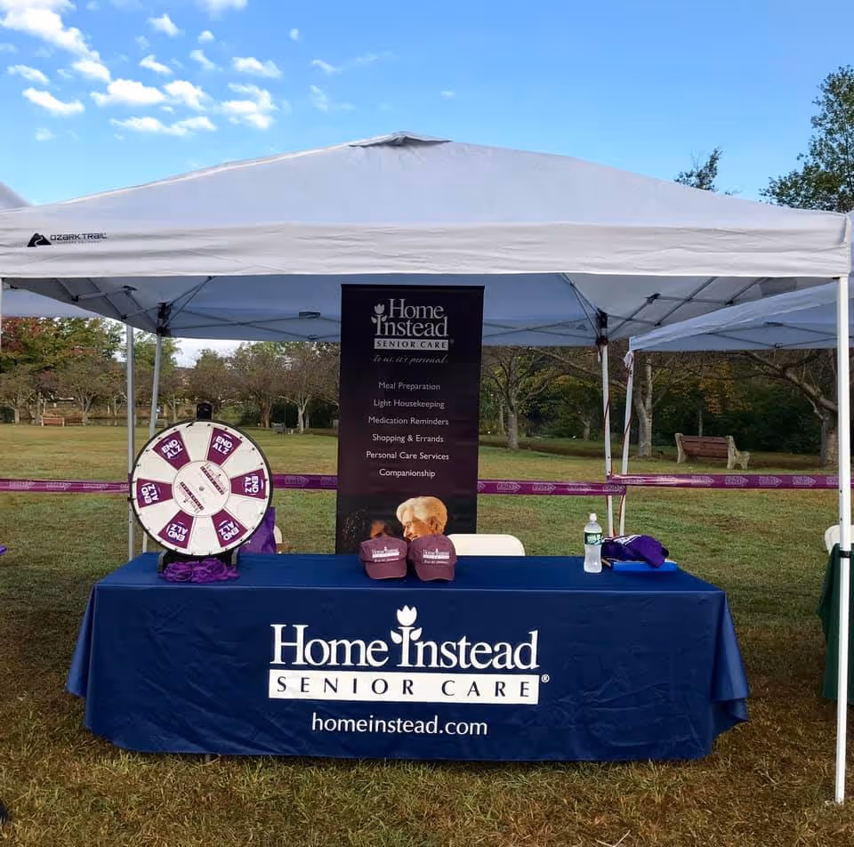 Outdoor booth under a white tent with Home Instead Senior Care branding and a prize wheel.