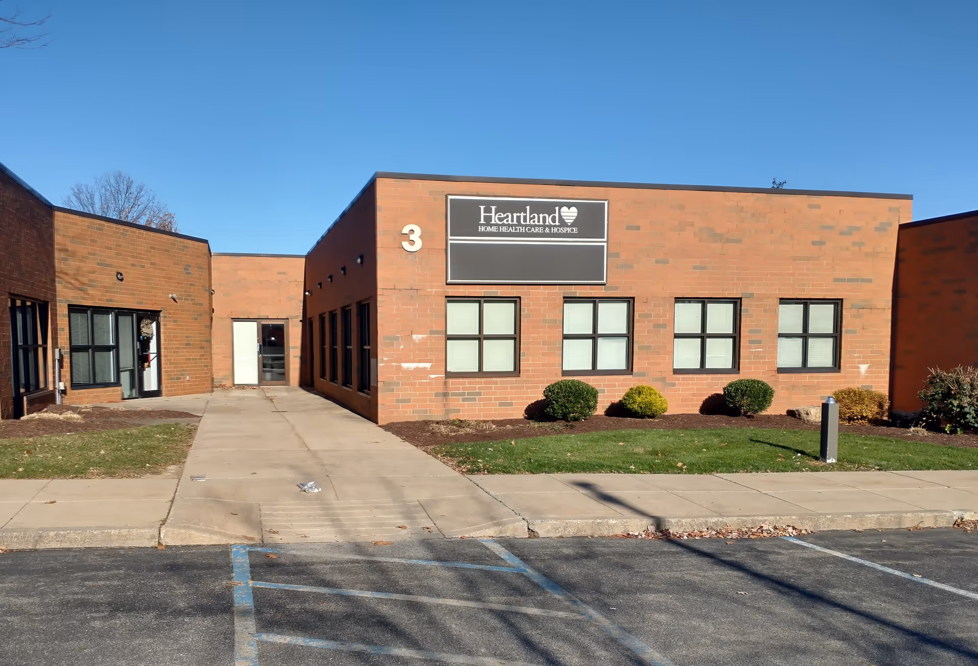 Brick building front with Heartland Hospice sign, several windows, and a parking area.